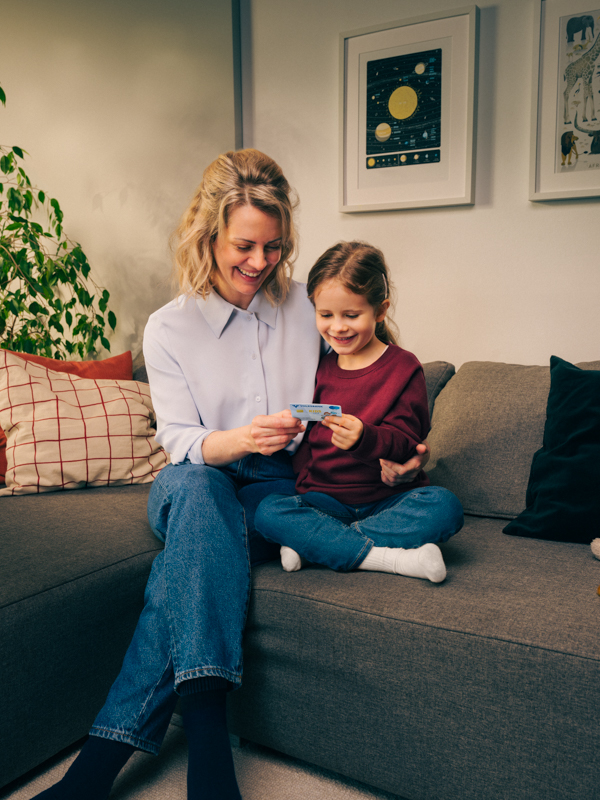 Mutter und Tochter sitzen auf der Couch und betrachten gemeinsam eine Volksbank Jugend Sparkarte.